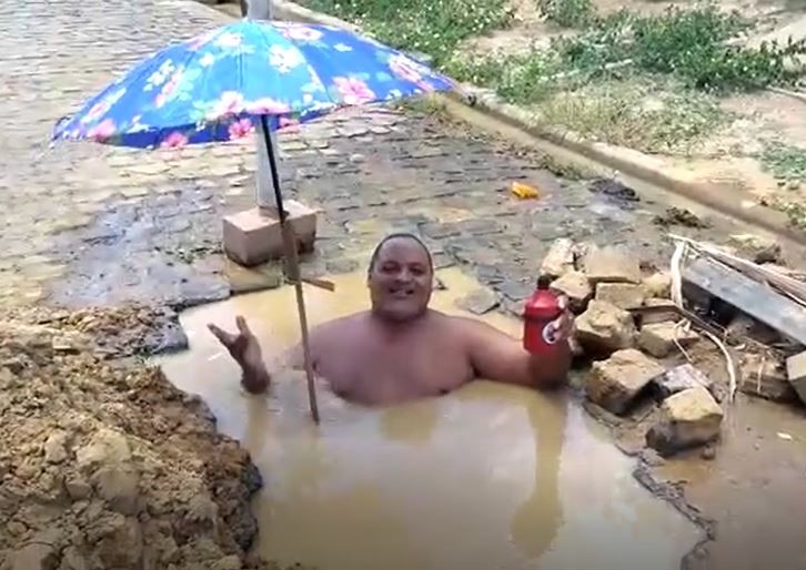 Morador toma banho dentro de buraco em rua do bairro Santa Clara.